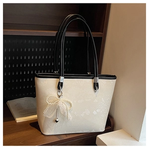 Close-up of cream tote bag with pearl lace charm and textured leather detail