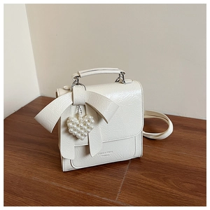 Detail of white pleated leather handbag with large bow and pearl heart charm accessory