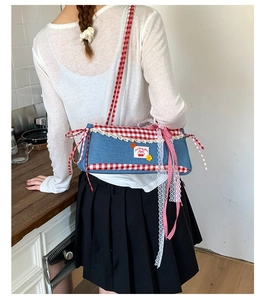 Detail of blue denim shoulder bag with red plaid trim, lace edges, and cherry patches