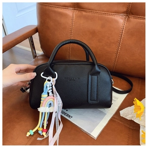 Close-up of black lychee leather Boston bag with rainbow charm and ribbon on leather sofa