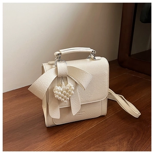 Detailed macro view of cream bow shoulder bag featuring pleated leather and pearl heart charm