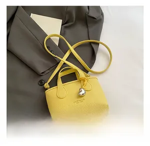Detail of bright yellow bucket bag with lychee grain leather and silver heart charm