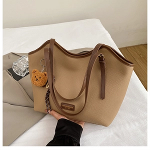 Close-up of khaki pebbled leather tote bag with brown straps and cute bear charm pendant