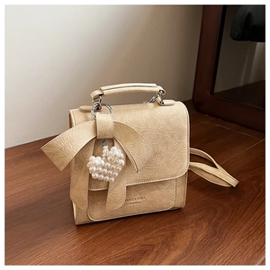 Detail of beige textured square bag with large bow and pearl heart charm on wood surface