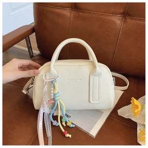 Detail view of cream-colored pebble leather boston bag with bohemian tassel charm accessory