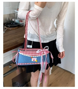 Detail of denim armpit bag with red gingham trim and lace bow decoration