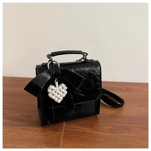 Detailed view of the black wrinkled texture, large bow, and pearl heart charm on the bag
