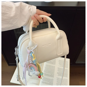 Close-up of white lychee leather handbag with rainbow charm and pearl ribbon detail