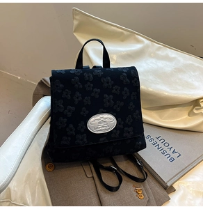 Detail aus schwarzem Blumen-Jacquard-Stoff und silberner Logoplakette auf dem Rucksack