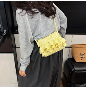 Detail showing pale yellow glossy crossbody bag with layered ruffle design on a model