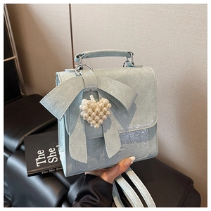 Close-up of light blue handbag with oversized bow and pearl heart pendant charm