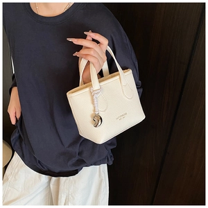 Dettaglio mini borsa a secchiello in pelle beige con manici e ciondolo a cuore