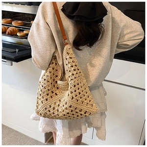 Close-up of beige hollow crochet straw tote bag with brown leather shoulder strap