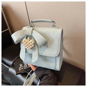 Detail of light blue bow handbag featuring ruffled texture and pearl heart charm