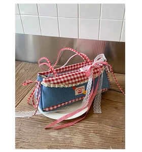 Detail of blue denim baguette bag with red gingham bows and cherry embroidery decoration