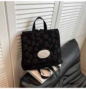 Detailansicht der schwarzen Blumen-Jacquard-Textur und Metallplakette auf dem Rucksack