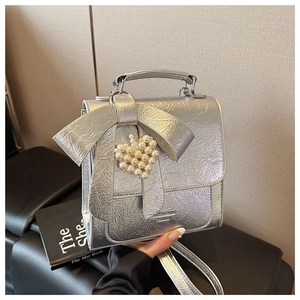 Close-up of a silver bow bag with crinkled texture and a pearl heart pendant accessory