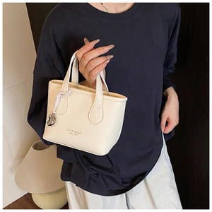 Dettaglio di una mini borsa a secchiello in pelle crema con ciondolo a cuore argentato