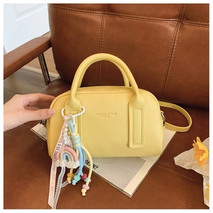 Detail of yellow boston bag featuring pebbled leather, rainbow charm and chic silk ribbon
