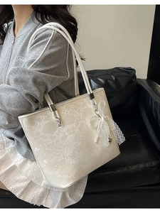 White snakeskin embossed tote bag with pearl lace charm shown in a side shoulder view