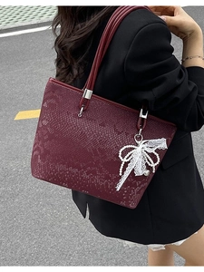 Burgundy snakeskin tote bag with pearl lace charm worn by a model on a city street