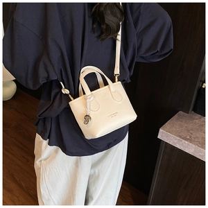 Detail of off-white tote bag with silver bean pendant and branded lettering logo