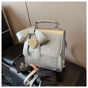 Detail of silver pleated bag with a large bow and pearl heart pendant held by a model