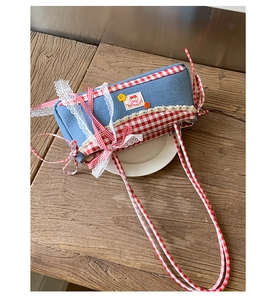 Close-up of blue denim shoulder bag featuring red plaid trim, lace edges, and cherry patch