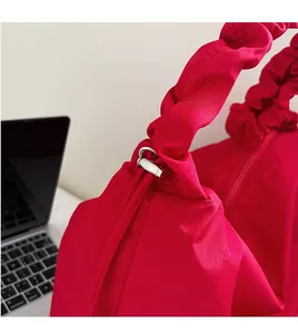 Macro detail of red canvas tote showing pleated shoulder strap and metal ring buckle