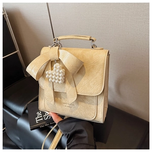 Detail of beige square crossbody bag with bow, pearl heart pendant, and textured leather
