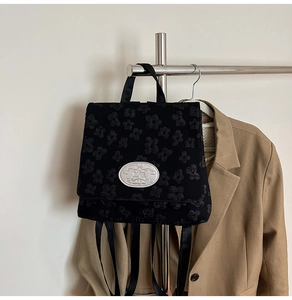 Detail eines schwarzen Rucksacks mit 3D-Floral-Jacquard und silberner Logoplakette