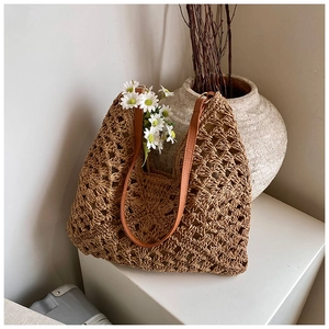 Close-up of woven hollow flower pattern and brown leather handle on straw tote bag