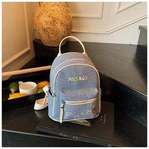Detail of mini denim backpack with MYBAG embroidery and colorful heart patches on stairs