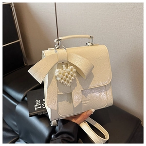 Detail of cream white patent leather bag featuring a bow and pearl heart pendant
