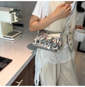 Detailed view of a silver ruffled crossbody bag worn by a model in a modern cafe setting