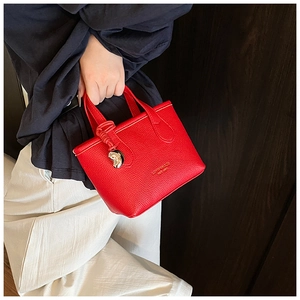 Detail of red litchi grain leather tote bag with a silver heart-shaped metal charm