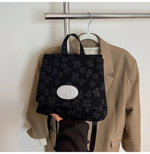 Detailansicht der schwarzen Blumen-Flocktextur und des silbernen Logos am Rucksack