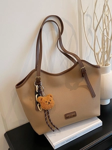 Khaki pebbled leather tote bag with brown straps and cute bear charm on white books