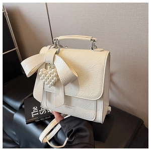 Detail of creamy white bow backpack with textured faux leather and pearl heart charm