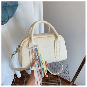 Close-up of cream Boston bag featuring pebble leather, embossed logo, and rainbow charm