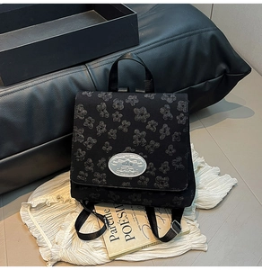 Detail eines schwarzen Rucksacks mit Blumenprägung und silberner Metall-Logoplatte