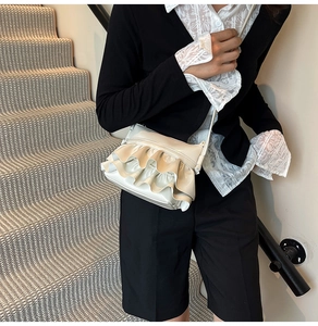 Detail view of cream ruffle layered crossbody bag on model with elegant styling