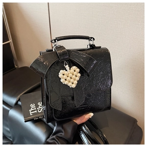 Close-up of black patent leather handbag featuring a large bow and pearl heart pendant