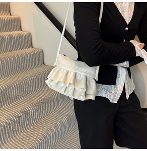 Close-up of white pleated ruffled shoulder bag in glossy leather worn by a model