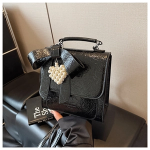 Detail of black patent leather bag with large bow and pearl heart pendant charm