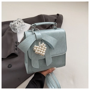 Detail view of light blue bow handbag with a pearl heart pendant and wrinkled leather texture