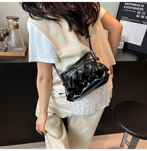 Close-up of black glossy ruched cloud crossbody bag with wavy pleated texture