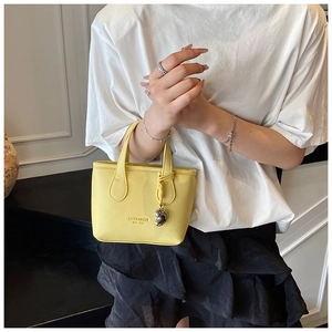 Dettaglio di una mini borsa a secchiello giallo brillante in pelle con ciondolo argento