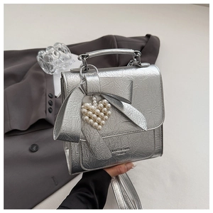 Macro shot of silver metallic bow bag with pearl heart charm and textured finish