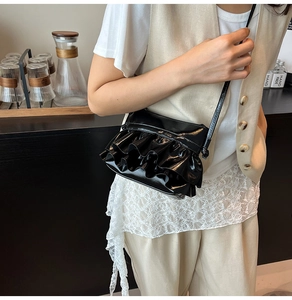Chic black patent leather crossbody bag with ruffled tiers and slim strap on model